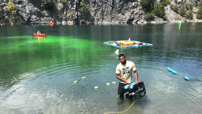 This image shows Bryan Bloomfield coming out of the water with an underwater robot.