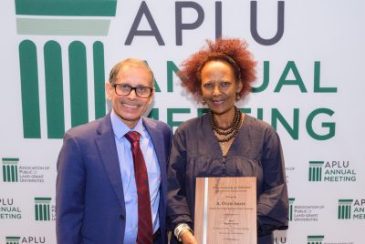 A man and a woman, holding an award, stand in front of a APLU sign smiling.
