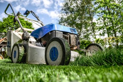 A blue lawnmower sits motionless on a patch of lush grass while blades of grass stick to the mower body.