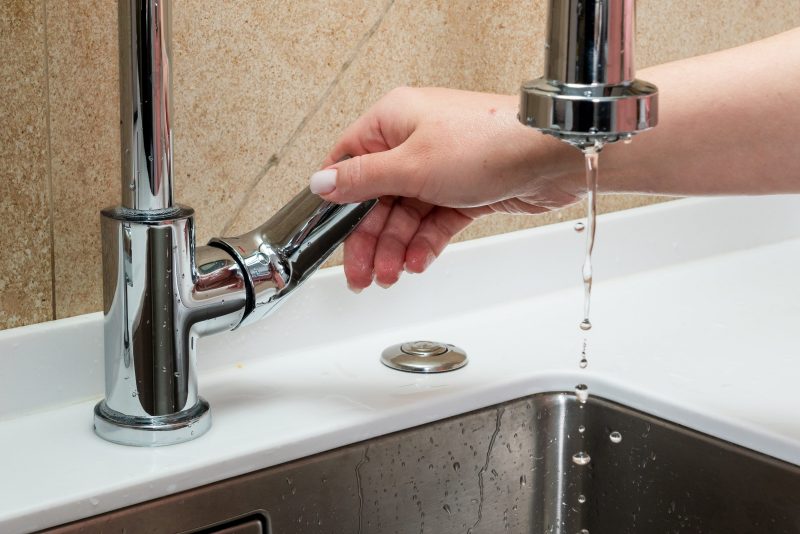 A hand turning on water at a kitchen sink.