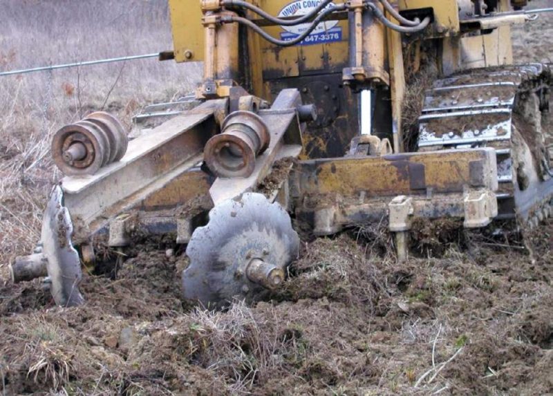 Figure 7. An advanced tillage tool intended for use on mined lands. A center shank (not visible) rips a deep trench through the compacted mine soil while the coulters produce a mound of loose soil over the rip where the trees are planted. Smaller shanks (up to six) to the right and left break up the surface on either side of the planting location to a depth of 12-to-18 inches; the top of one such smaller shank is visible as it enters the soil on the right hand side of the tool bar.