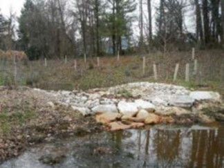 A shallow pool of water in the foreground ends at a mound of boulders and stones. A second pool is seen in the background, behind the mound.