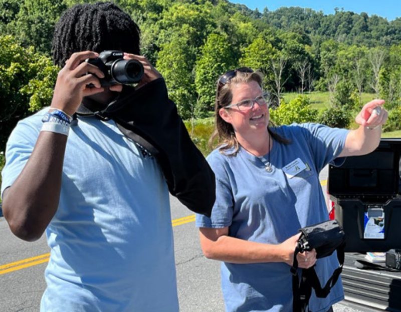 A volunteer points ahead while a student aims a camera