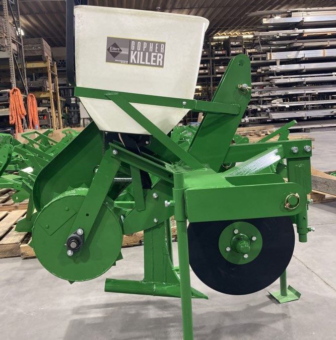 A large green tractor implement with a feeder labeled Gopher KillerŽ on top.