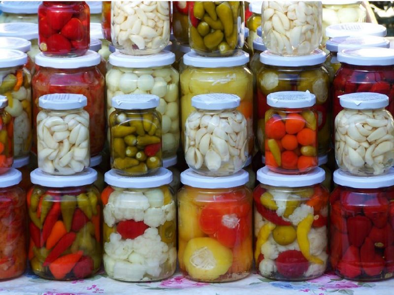 Photo of jarred pickled vegetables of various colors from red, white, green, and yellow, that are stacked on top of each other.