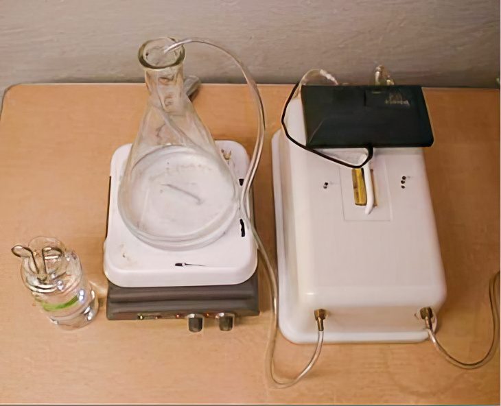 Clear tubing exiting a plastic box and entering a beaker on top of a small piece of equipment.