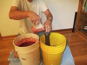 crushed blackberries being poured in a nylon bag in a 5-gallon bucket