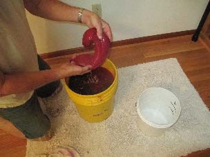 filled nylon bag being removed from a 5-gallon bucket of liquid.