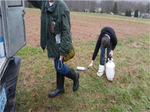 Figure 4, A person spraying the boots of another person with a hand pump sprayer.