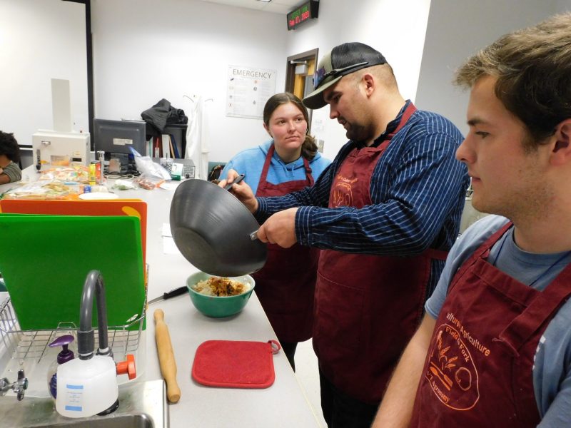 Zach DeBush (center) and classmates prepare Thai basil chicken. Photo by Patrick McKee for Virginia Tech.